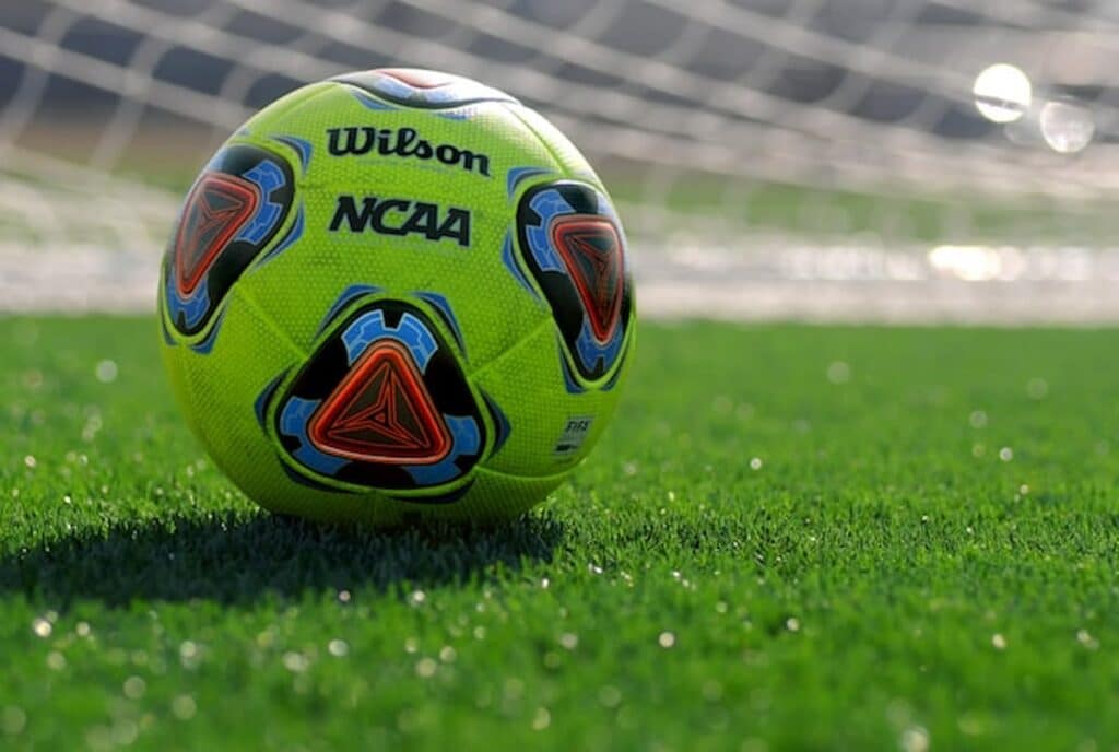 Bright yellow soccer ball on green turf in front of goal