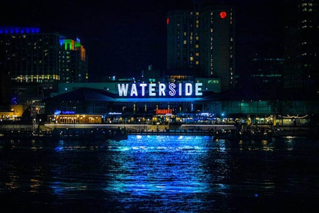 Neon sign reflecting over city waterfront at night