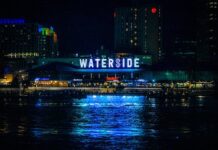 Neon sign reflecting over city waterfront at night