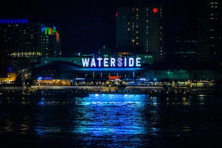 Neon sign reflecting over city waterfront at night