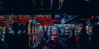 People sitting at rows of gaming machines in a dimly lit arcade.