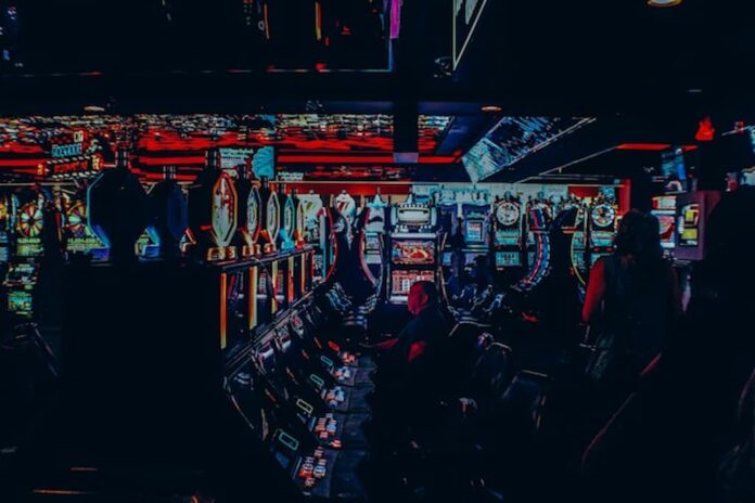 People sitting at rows of gaming machines in a dimly lit arcade.