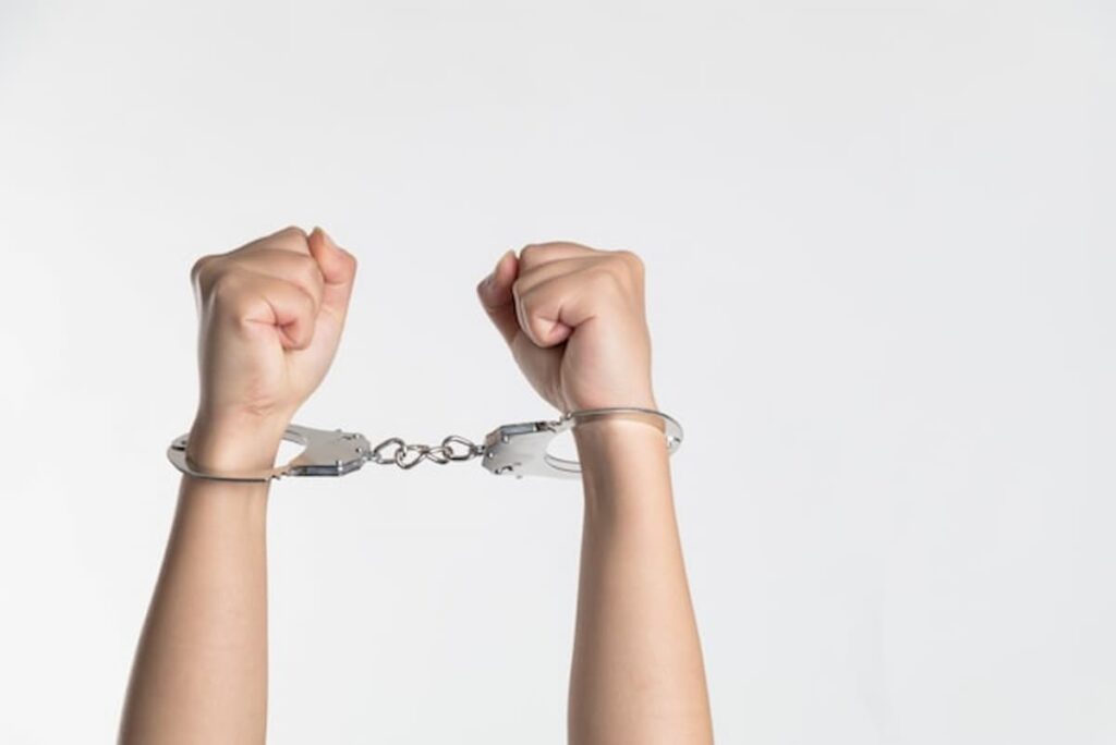 Hands raised in metal handcuffs against a white background.