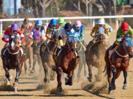 Jockeys and horses racing on a dirt track during a daytime horse-racing event.