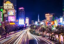 Long-exposure night view of the Las Vegas Strip showing casino lights, hotel signs, and traffic streaks.