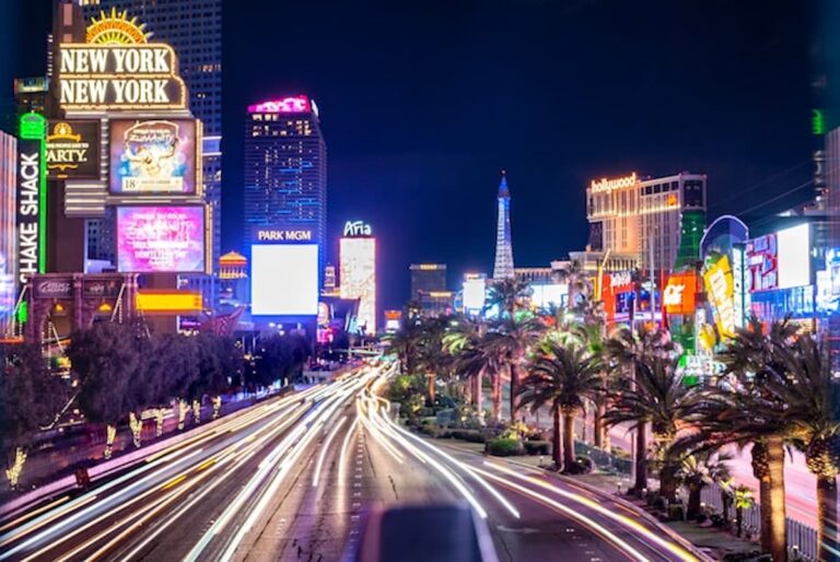 Long-exposure night view of the Las Vegas Strip showing casino lights, hotel signs, and traffic streaks.