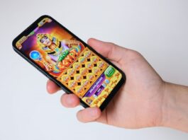 Light & Wonder Reports Record iGaming Results Amid Social-Casino Headwinds & NASDAQ Exit A person holding a smartphone displaying a colorful online slot game.