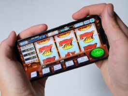 VGW is Preparing to Launch Two New Sweepstakes Casinos: LuckyLand Casino & United Slots Hands holding a smartphone displaying a generic online slot machine game