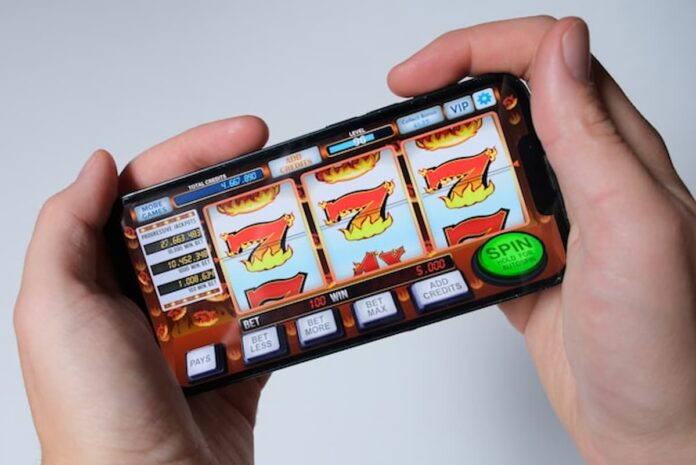 VGW is Preparing to Launch Two New Sweepstakes Casinos: LuckyLand Casino & United Slots Hands holding a smartphone displaying a generic online slot machine game