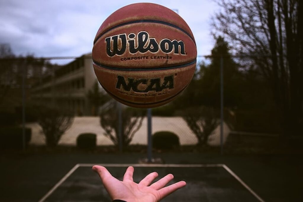 A person tossing an NCAA basketball on an outdoor court.