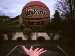 A person tossing an NCAA basketball on an outdoor court.