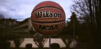 A person tossing an NCAA basketball on an outdoor court.
