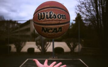 A person tossing an NCAA basketball on an outdoor court.