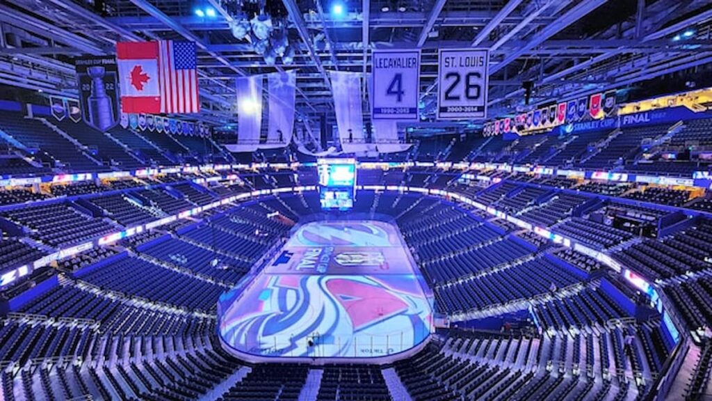 Empty NHL arena before a Stanley Cup Final game, lit in blue with team banners hanging overhead.