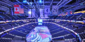 Empty NHL arena before a Stanley Cup Final game, lit in blue with team banners hanging overhead.