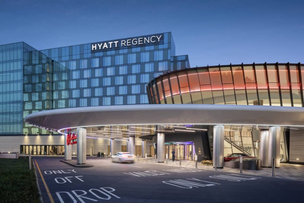Rendering of the Resorts World New York City at Aqueduct Racetrack, showing the connected Hyatt Regency hotel and main casino entrance at dusk.