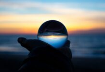 A hand holding a clear glass ball on a beach at dusk