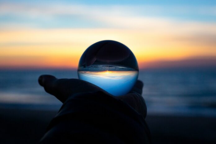 A hand holding a clear glass ball on a beach at dusk