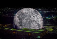 A high-resolution aerial photo of the Las Vegas Sphere lit up as a massive moon, set against the city’s night skyline.