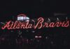 Neon Atlanta Braves sign glowing at night with visitors walking underneath.