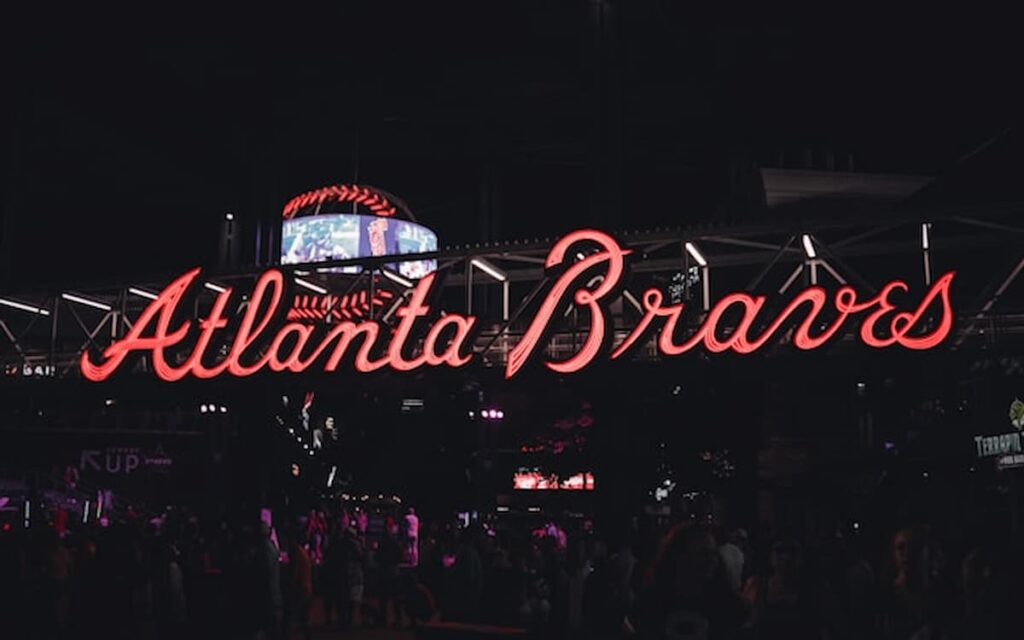 Neon Atlanta Braves sign glowing at night with visitors walking underneath.