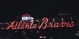 Georgia Tourism Committee Quietly Recommends Mobile Sports Betting in Final Report Neon Atlanta Braves sign glowing at night with visitors walking underneath.