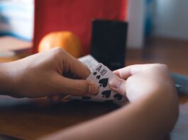 Latin Business Association Joins Cardroom Coalition to Oppose Proposed California Regulations Person holding a pair of spade cards during a card game at a table.