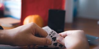 Latin Business Association Joins Cardroom Coalition to Oppose Proposed California Regulations Person holding a pair of spade cards during a card game at a table.