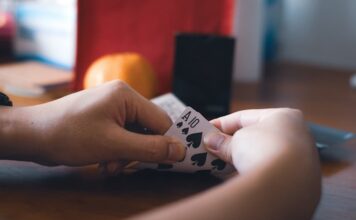 Latin Business Association Joins Cardroom Coalition to Oppose Proposed California Regulations Person holding a pair of spade cards during a card game at a table.