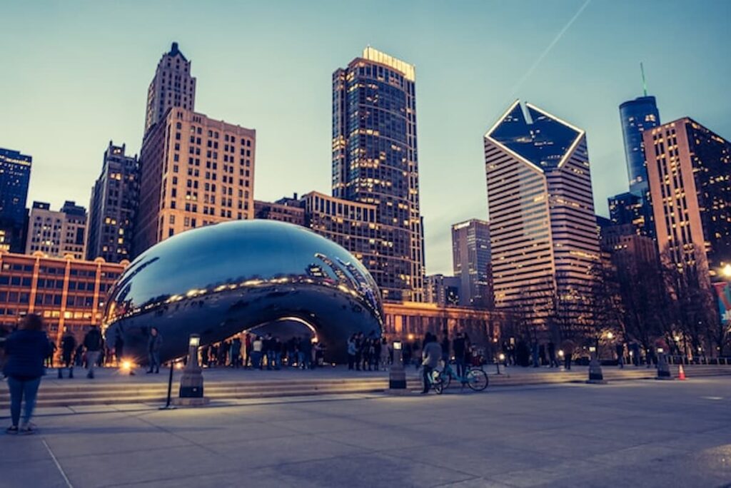 A view of Chicago’s downtown skyline at dusk with the Cloud Gate sculpture in Millennium Park and pedestrians in the foreground.