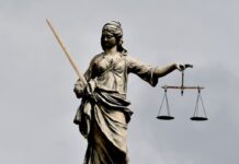 Two Federal Courts Allow ‘Risk-Free’ Lawsuits Against DraftKings to Proceed A stone statue of Lady Justice stands against a cloudy sky, holding a sword in one hand and a set of scales in the other.