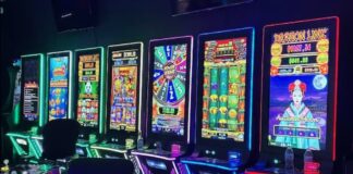 Illegal Gambling Operation Disguised as Repair Shop Shut Down in Florida’s Orange County A row of illuminated slot-style gaming machines with colorful screens and chairs lined up in a dark room.