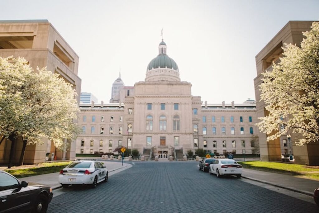 Exterior view of the Indiana Statehouse in Indianapolis with police cars parked in front and spring trees in bloom