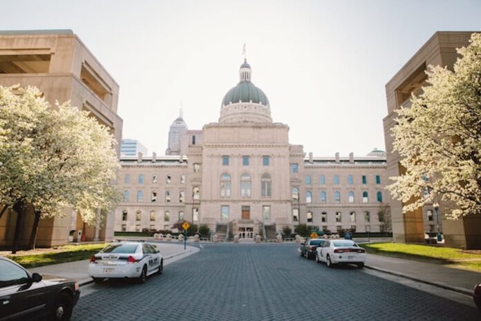 Indiana Bill Targets Online Sweepstakes Casinos With New Definition, $100K Penalties Exterior view of the Indiana Statehouse in Indianapolis with police cars parked in front and spring trees in bloom