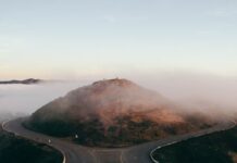 A mountain road dividing into two separate paths on a foggy hillside.