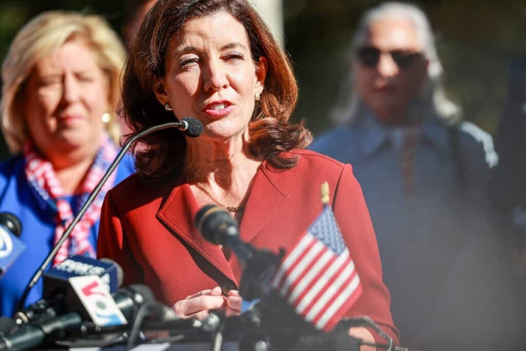 New York Governor Kathy Hochul speaking at a press conference with microphones in front of her.