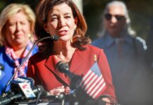 New York Governor Kathy Hochul speaking at a press conference with microphones in front of her.