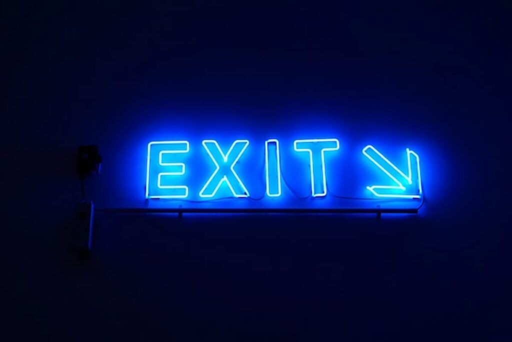 Blue neon “Exit” sign with an arrow pointing right against a dark background