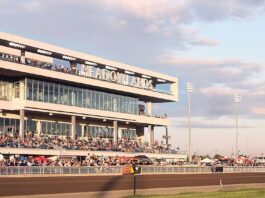 Crowds gathered in the grandstand at the Meadowlands Racetrack during a live racing event at sunset.