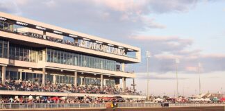 Crowds gathered in the grandstand at the Meadowlands Racetrack during a live racing event at sunset.