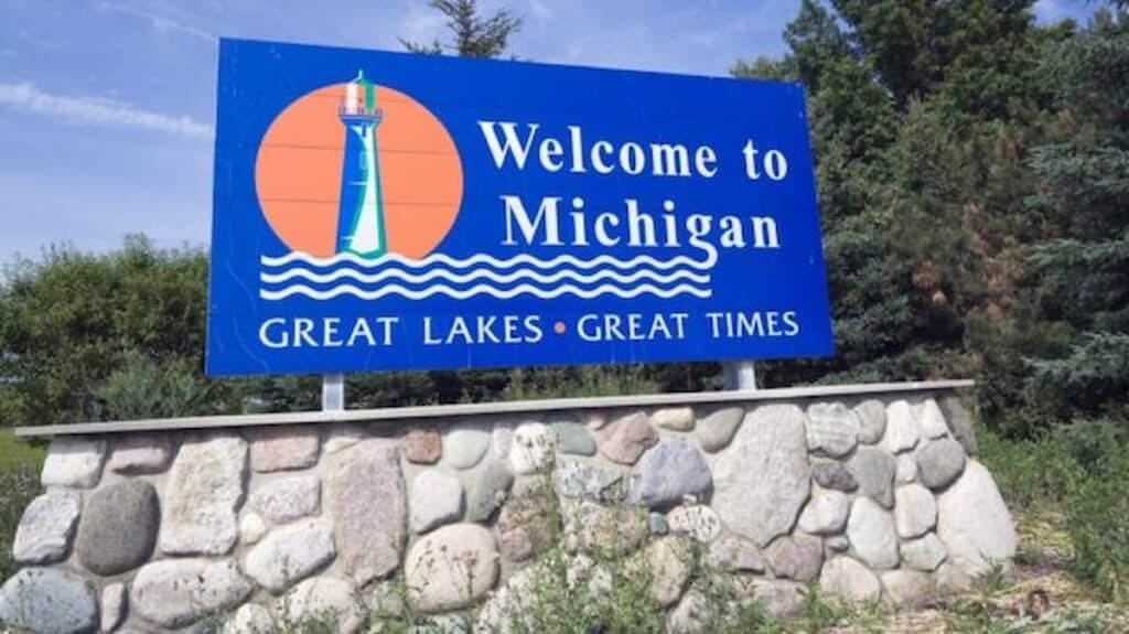Blue “Welcome to Michigan” road sign with a lighthouse illustration and the slogan Great Lakes Great Times.