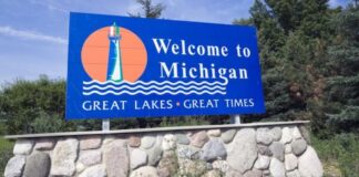 Blue “Welcome to Michigan” road sign with a lighthouse illustration and the slogan Great Lakes Great Times.