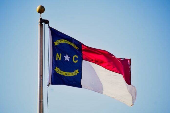 North Carolina state flag flying on a flagpole against a clear blue sky