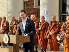 Alabama Gambling Reform Returns to Focus as Rep. Ensler Signals a Push as Lieutenant Governor Alabama state Rep. Phillip Ensler speaks at a campaign event outside a government building, standing at a podium with a group of Buddhist monks behind him.
