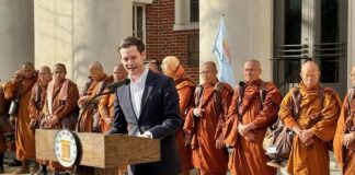 Alabama Gambling Reform Returns to Focus as Rep. Ensler Signals a Push as Lieutenant Governor Alabama state Rep. Phillip Ensler speaks at a campaign event outside a government building, standing at a podium with a group of Buddhist monks behind him.