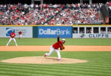 A Cleveland Guardians pitcher delivers a pitch from the mound during a daytime MLB game with a full crowd in the stands.