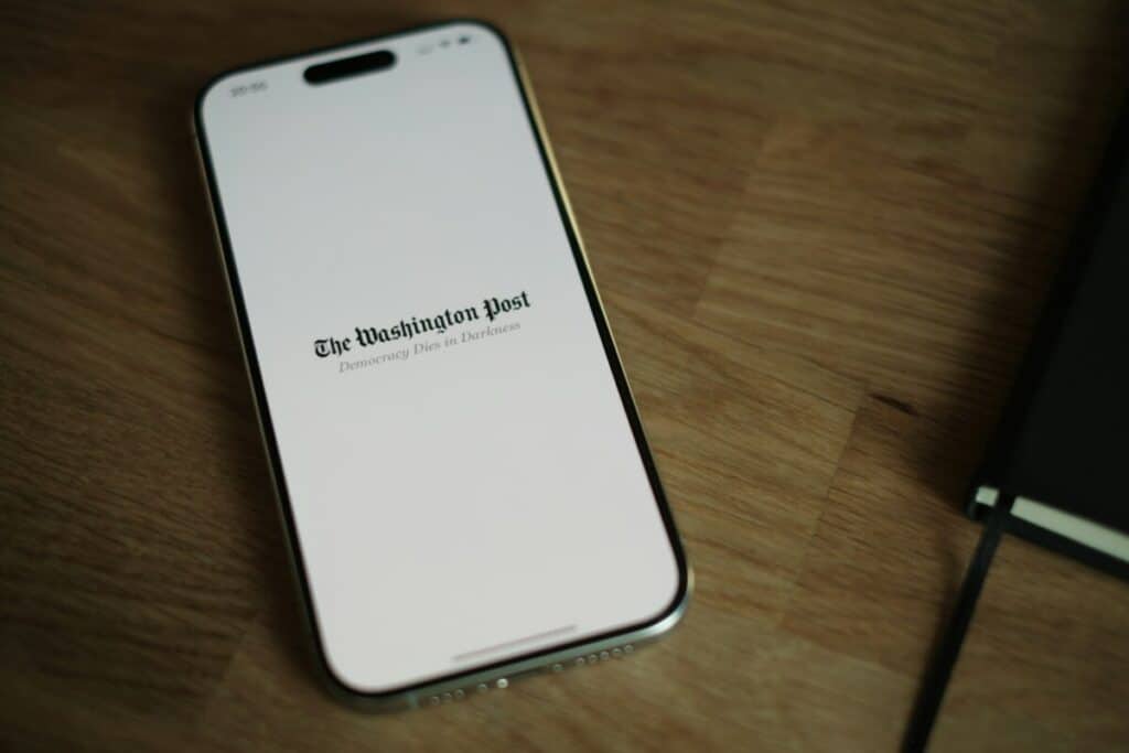 A smartphone displaying The Washington Post logo on a wooden surface