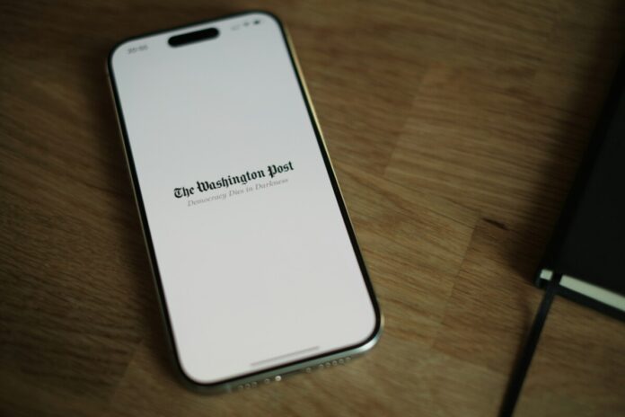 A smartphone displaying The Washington Post logo on a wooden surface