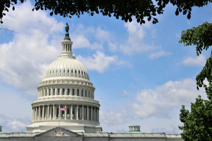 The U.S. Capitol building in Washington, D.C., seen beneath a blue sky with trees framing the dome.