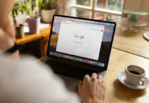 Google Opens Ad Platform to U.S. Prediction Markets A person using a laptop displaying the Google homepage while sitting at a table with a cup of coffee.